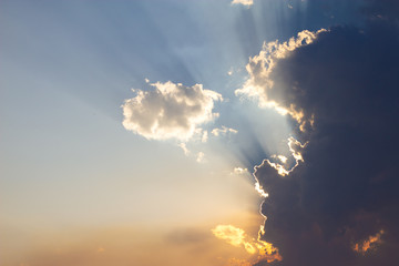 sky in shades of blue and yellow illuminated by sun rays clouded by clouds