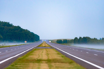 Morning before sunrise. The long highway goes into the distance. Misty fields at the edge of the road.