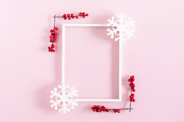 Christmas modern composition. Xmas decorations, photo frame, red berries, snowflakes on pastel pink background. Christmas, New Year, winter concept. Flat lay, top view, copy space