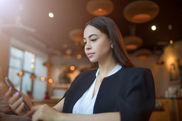 Young serious woman successful fashion blog writer publication article on web page via mobile phone during lunch break in restaurant. Confident business female online booking via cell telephone