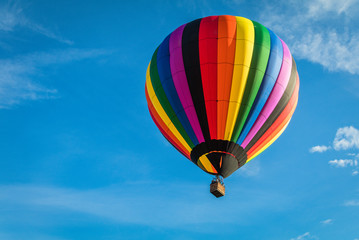 Rainbow colorful hot-air balloon floats on a summer morning with bright blue sky 