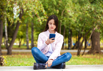 Brunette girl photographs herself on a cell phone while sitting in an autumn park.