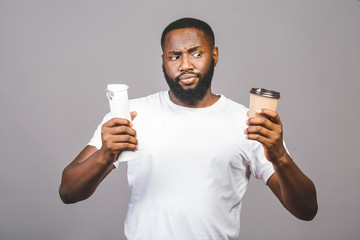 Zero waste concept. Young african american man making choose between cup of coffee and recycle one standing over isolated grey background.