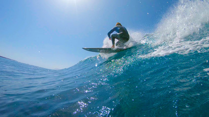 Fototapeta na wymiar LOW ANGLE VIEW Male surfboarder riding and carving cool barrel wave near volcano