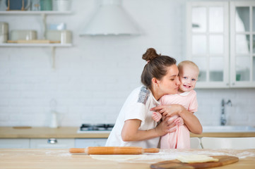 Obraz na płótnie Canvas mom hugs little daughter in the kitchen, eyes closed with tenderness
