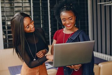two beautiful and stylish young, dark girls standing in a restaurant and using a laptop