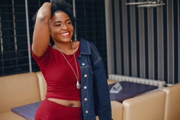 young and beautiful dark-skinned girl with curly dark hair in a red dress standing in a cafe