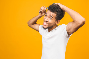 Fototapeta na wymiar Portrait of handsome young african american black man combing his hair in bathroom. Isolated over yellow background.