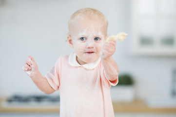 blue-eyed girl with a face in flour holds a piece of dough in his hand
