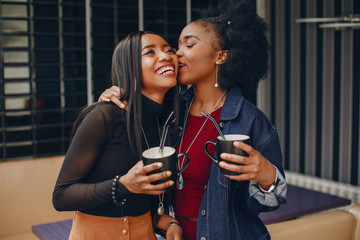 two beautiful and stylish young, dark girls standing in a restaurant and drinking a coffee