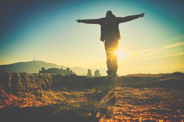 victorious male person with spreaded hands is enjoying panorama of beautiful nature in Belogradchick in Bulgaria with sun on the background. Vintage image.