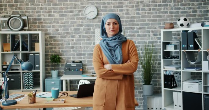 Portrait of ambitious mixed race woman in hijab standing in office with arms crossed and looking at camera with serious face. People and modern lifestyle concept.