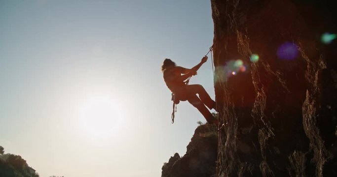 Professional caucasian alpinist is climbing up a cliff during hot day, using special equipment - extreme tourism concept 4k footage