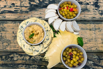 Snack plates with Humus and olives placed on bowls and blue cheese sliced on a wooden table, top view.