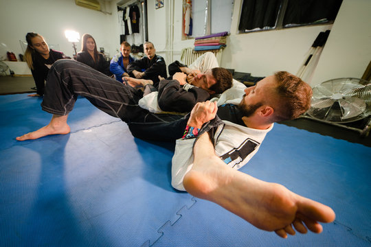 Wide angle black or brown belt BJJ brazilian jiu jitsu fighter in training sparing attacking from dominant position going for the choke at the martial arts academy training class teaching technique