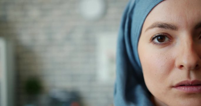 Close-up portrait of attractive Muslim woman in hijab half face on brick wall background looking at camera alone. Youth, people and lifestyle concept.
