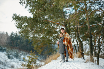 happy couple wrapped in a blanket standing in the park on a snowy day