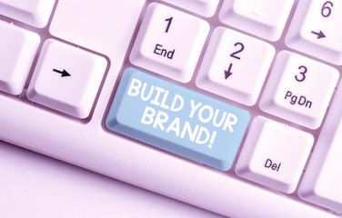 Conceptual hand writing showing Build Your Brand. Concept meaning creates or improves customers knowledge and opinions of product White pc keyboard with note paper above the white background