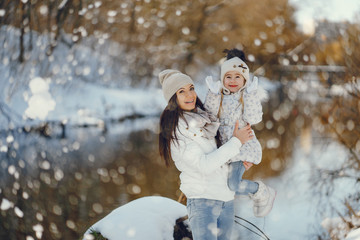 young and stylish mom with long dark hair playing with her little cute daughter in winter snow park standing near water