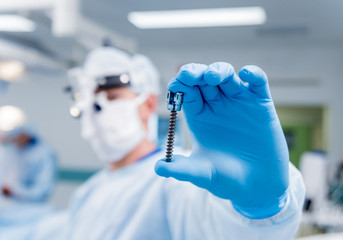 Spinal surgery. Surgeon show polyaxial screw in operating room with surgery equipment. Laminectomy. Spine fixation systems