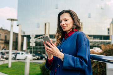 Office buildings city people in suit. Caucasian businesswoman using smartphone with hand. Business concept. Portrait stylish business woman in fashionable clothes holding Phone near office building