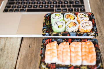 Tasty sushi rolls, shrimp and laptop at wooden table. Food delivery. Workspace at home