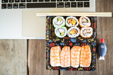 Tasty sushi rolls, shrimp and laptop at wooden table. Food delivery. Workspace at home