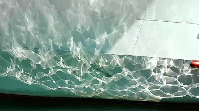 Close up to the reflection of sunlight on the bottom of a white boat docked