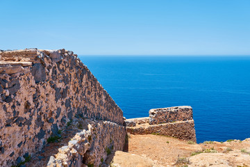 Fototapeta na wymiar Ruins of old historical wall with blue sea and horizon on a background in Crete, Greece. Copy space. 