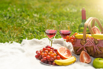 A bottle of red wine with glasses and fruit on a green meadow. Picnic and relaxation on nature. Sunny and bright mood.