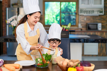 Happy asian family in the kitchen.Mother and son help to make vegetable salad.Mom teaching kid boy cooking healthy salad for dinner.