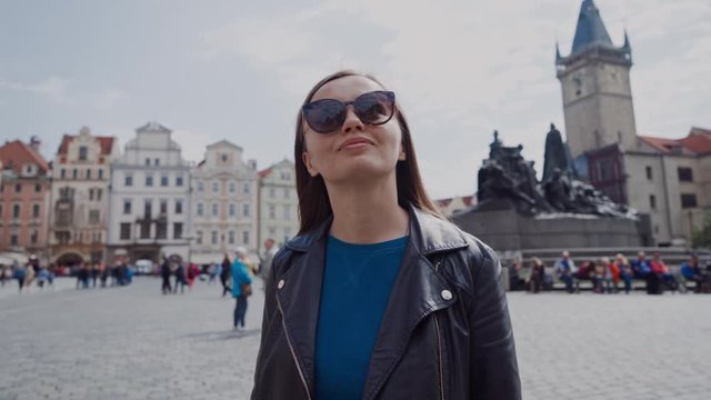 Stylish young girl in sunglasses walks on Old Town Square in Prague, Czech Republic. There is Jan Hus Monument on the background. Beatiful sunny day. Beautiful Young Woman Tourist In Prague