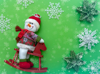 Smiling snowman toy in winter clothes, green red, white Christmas background, snowflakes, template for greeting card with free space for text