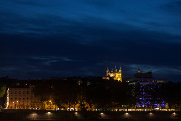 Panorama of Colline de Fourviere Hill at night seen from the riverban of the Rhone river. Notre Dame de Fourviere, the main basilica church of the city, is visible