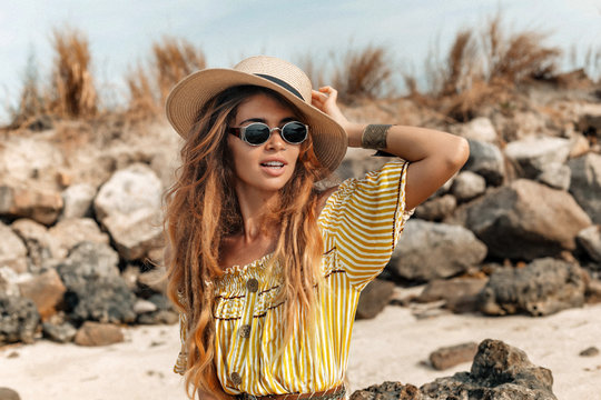 beautiful young stylish boho woman in elegant dress outdoors wearing hat and sunglasses at sunset