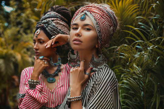 portrait of two beautiful stylish woman wearing turban on tropical background