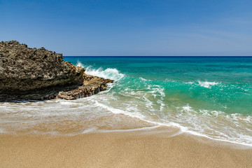 Ocean foamy waves at the beach near rocks, crystal clear turquoise water, Sosua, Puerto Plata, Dominican Republic