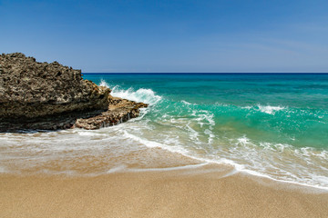 Fototapeta na wymiar Ocean foamy waves at the beach near rocks, crystal clear turquoise water, Sosua, Puerto Plata, Dominican Republic