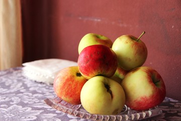 red and yellow apples in a crystal dish on the table, in warm beige tones, backlighting