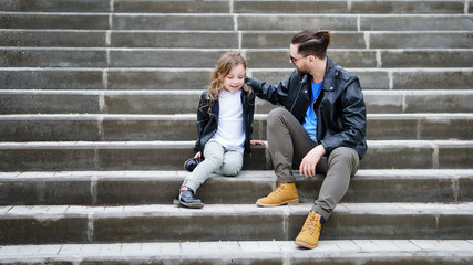 Fashionable stylish family portrait for a walk. Dad and daughter posing on the city stairs. Excursion. Travel and tourism concept. Time together. Family look. Urban casual outfit. 