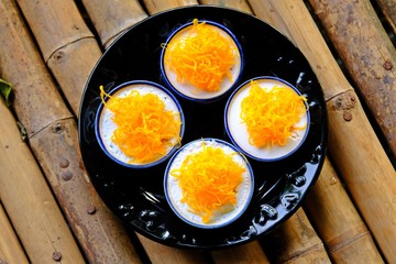 Top view cups of coconut milk custard topped with angel's hair(egg threads) placed in black plate on bamboo table.