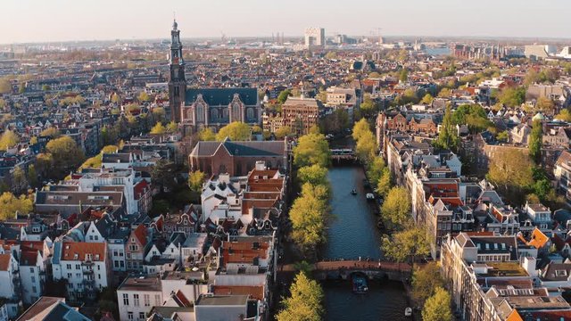 Amsterdam, Netherlands: drone view of Westerkerk church and narrow canal with bridges and boats traffic