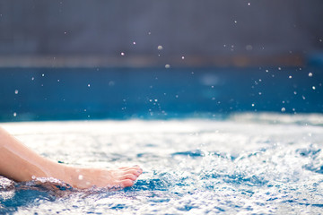Closeup image of legs and bare feet kicking and splashing water in the pool
