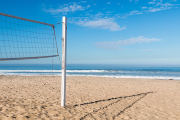 Volleyball net on a sand court with the ocean in the background.
