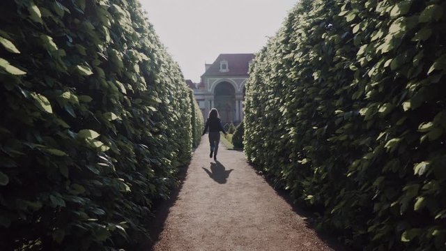 Young woman running in the green park labyrinth in evening sunshine. Back view. Wallenstein Garden in Prague
