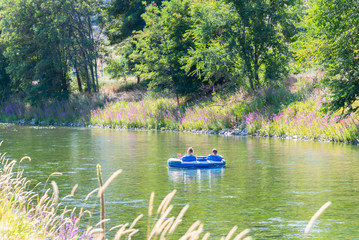 Man and woman float down Penticton River Channel on two-person inner-tube in summer