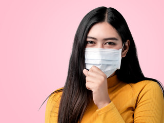Asian woman wearing yellow sweater and coughing with mask on pink background.
