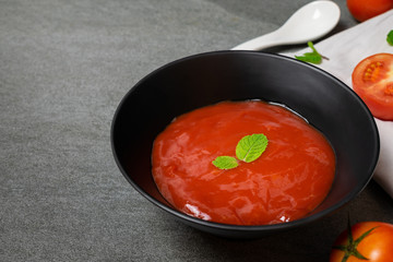 Tomato sauce and mint leaves in black bowl with tomatoes sliced on concrete table.