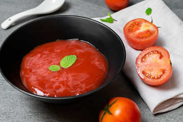 Tomato sauce and mint leaves in black bowl with tomatoes sliced on concrete table.