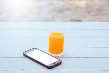 Orange juice in glass and mobile phone on white wooden table